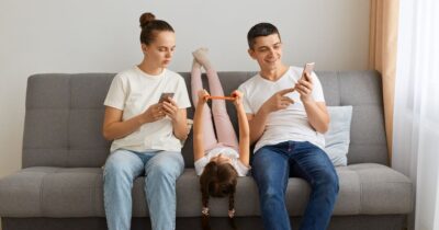 A woman and man next to their child on a couch looking at their email on mobile phone and comparing options