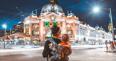 A woman with a baby on her back looking at Flinders St in Melbourne Australia like the choice of Australian web host vs overseas providers